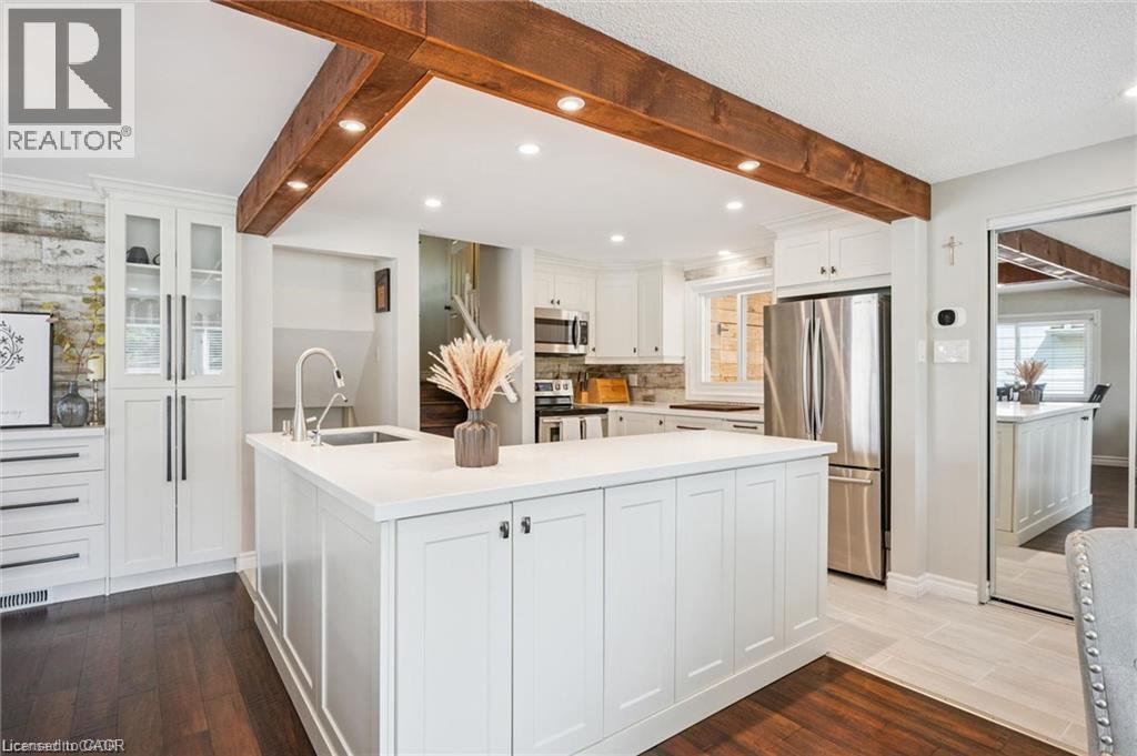 Gourmet kitchen featuring a large waterfall-edge island with white cabinetry, stainless steel appliances, and a professional-grade sink with pull-down faucet - 659 Glen Forrest Boulevard, Waterloo, ON - Indoor Photo Showing Kitchen With Upgraded Kitchen