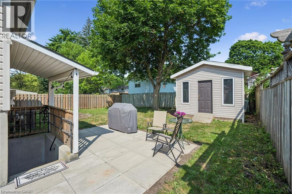 Expansive backyard oasis featuring a mature shade tree, manicured lawn, and multiple entertaining spaces including a covered patio with wooden railings and a detached accessory dwelling - 659 Glen Forrest Boulevard, Waterloo, ON - Outdoor With Deck Patio Veranda