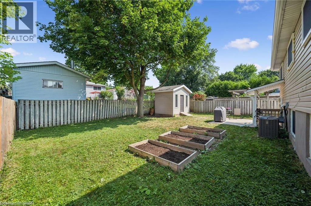 Expansive backyard oasis featuring a level, manicured lawn, mature shade trees, raised garden beds, detached storage shed with pitched roof, white vinyl fencing, and mature landscaping - 659 Glen Forrest Boulevard, Waterloo, ON - Outdoor