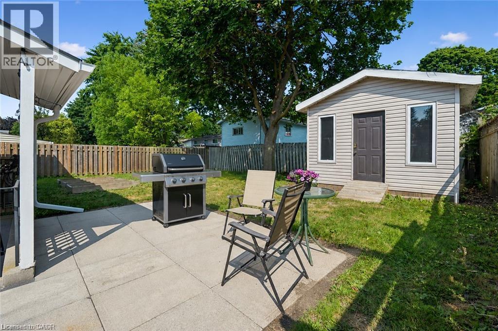 Expansive backyard featuring a concrete patio, mature trees, wood fence, and an outdoor shed with siding and multiple windows - 659 Glen Forrest Boulevard, Waterloo, ON - Outdoor