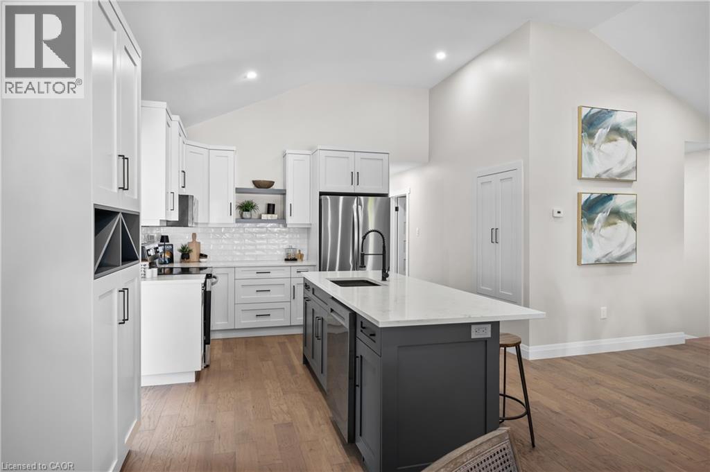 Modern kitchen featuring white cabinetry with brushed metal hardware, stainless steel appliances including a refrigerator and range hood, quartz countertops, a contrasting black kitchen island with se - 1041 Shepherd'S Drive, Burlington, ON - Indoor Photo Showing Kitchen With Upgraded Kitchen
