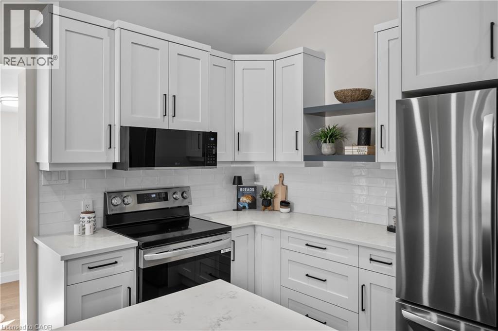 Modern kitchen featuring white shaker-style cabinetry with black hardware, stainless steel appliances including a slide-in range and refrigerator, white subway tile backsplash, and light-filled counte - 1041 Shepherd'S Drive, Burlington, ON - Indoor Photo Showing Kitchen With Upgraded Kitchen