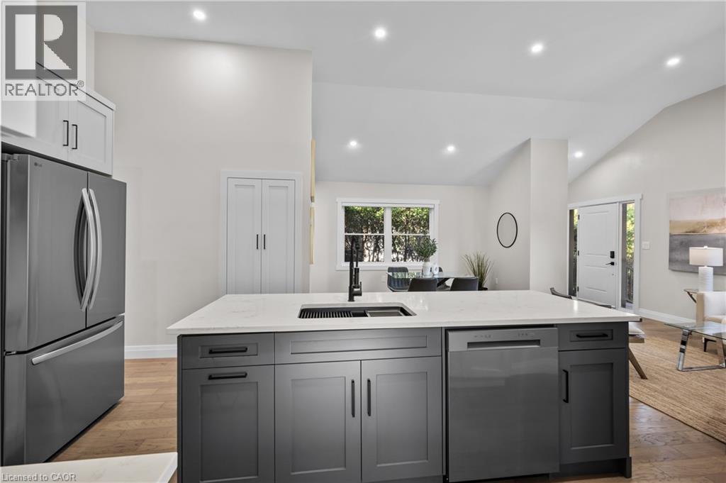Contemporary kitchen featuring a large waterfall-edge island with integrated sink, matte black cabinetry with modern hardware, stainless steel French-door refrigerator, recessed ceiling lighting, and - 1041 Shepherd'S Drive, Burlington, ON - Indoor Photo Showing Kitchen With Upgraded Kitchen