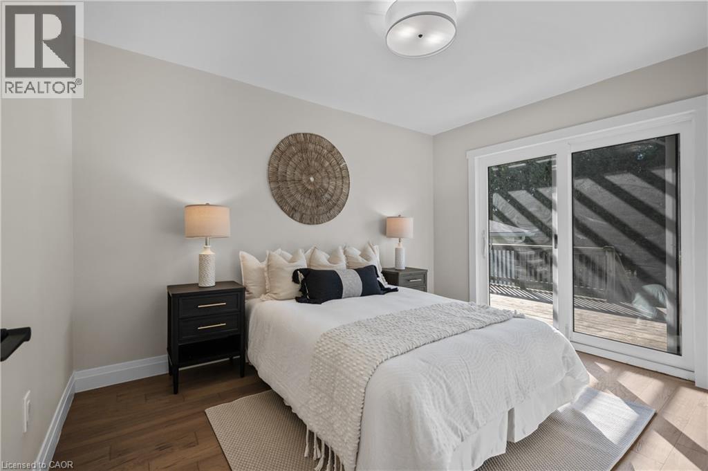 Bright primary bedroom featuring wood-finish flooring, a queen-size bed with upholstered headboard, dual nightstands with integrated lighting, and sliding glass doors opening to a private balcony with - 1041 Shepherd'S Drive, Burlington, ON - Indoor Photo Showing Bedroom