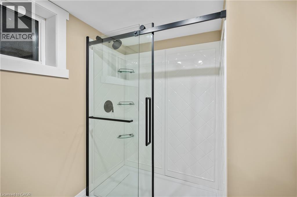 Modern frameless glass shower enclosure with sleek matte black hardware and sliding glass doors, featuring multiple showerheads and integrated shelving - 1041 Shepherd'S Drive, Burlington, ON - Indoor Photo Showing Bathroom