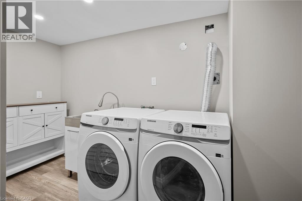Laundry area featuring wood-finish flooring, recessed lighting, white cabinetry with dark hardware, and a utility sink with a gooseneck faucet - 1041 Shepherd'S Drive, Burlington, ON - Indoor Photo Showing Laundry Room