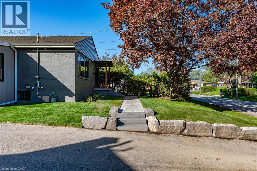 Stone retaining wall with a paved driveway, stone walkway, and sloped lawn - 1041 Shepherd'S Drive, Burlington, ON - Outdoor