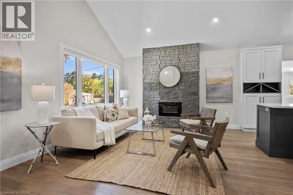 Vaulted ceiling, stone-clad fireplace, wood-finish flooring, built-in cabinetry, and large picture windows - 1041 Shepherd'S Drive, Burlington, ON - Indoor Photo Showing Living Room With Fireplace
