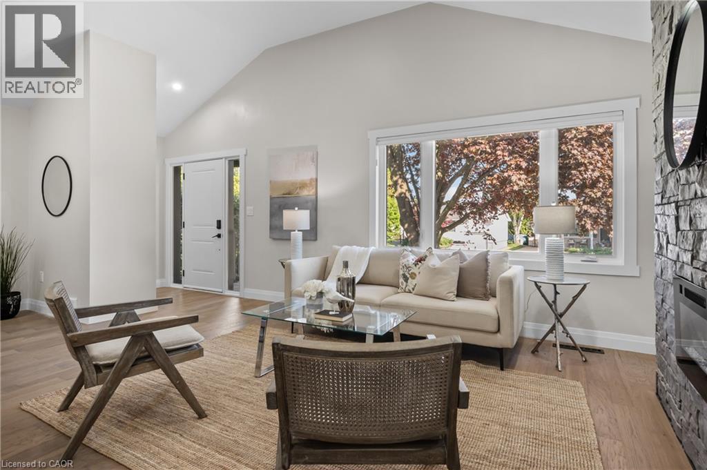 Vaulted ceiling, wood-finish flooring, stone-clad fireplace, large window, and white interior door - 1041 Shepherd'S Drive, Burlington, ON - Indoor Photo Showing Living Room