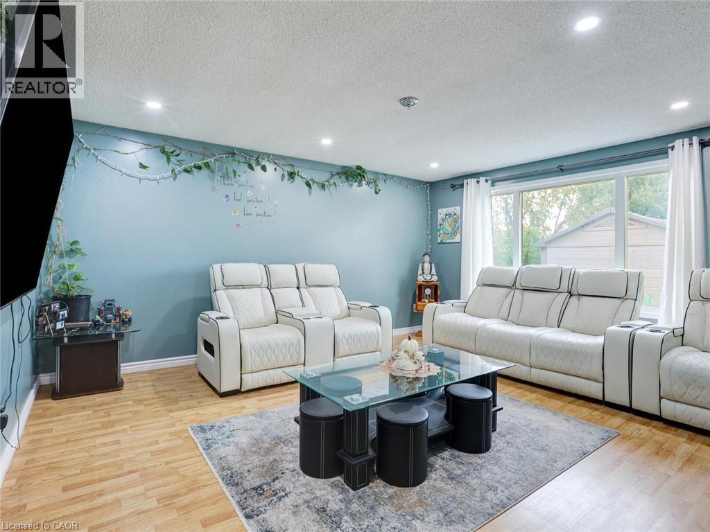 Sophisticated living room showcasing dual cream-upholstered sectional sofas with integrated recliners, wood-finish flooring throughout, and soft ambient recessed lighting - 128 Macatee Place, Cambridge, ON - Indoor Photo Showing Living Room