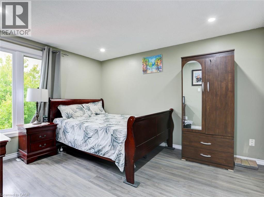 Spacious bedroom featuring a wood-finish sleigh bed, coordinating wood nightstand and wardrobe, recessed ceiling lighting, and expansive glass sliding doors with natural light - 128 Macatee Place, Cambridge, ON - Indoor Photo Showing Bedroom