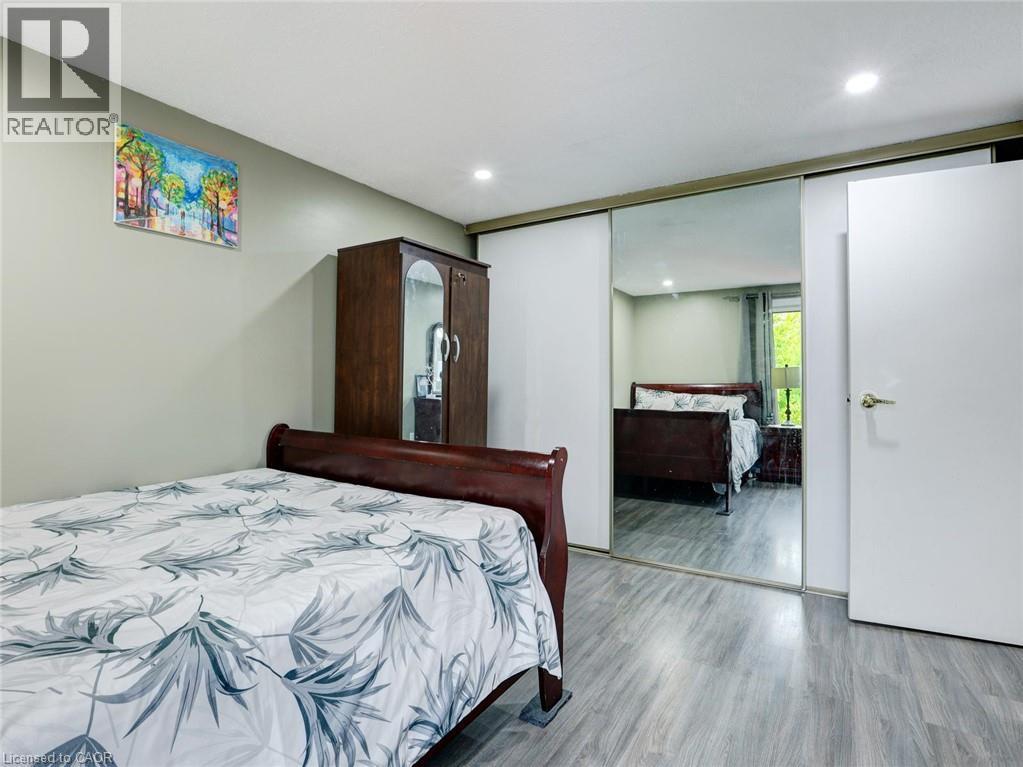 Recessed ceiling lighting, light gray wall color, wood-finish flooring, white sliding closet doors, and a white interior door with a brass-finish handle - 128 Macatee Place, Cambridge, ON - Indoor Photo Showing Bedroom