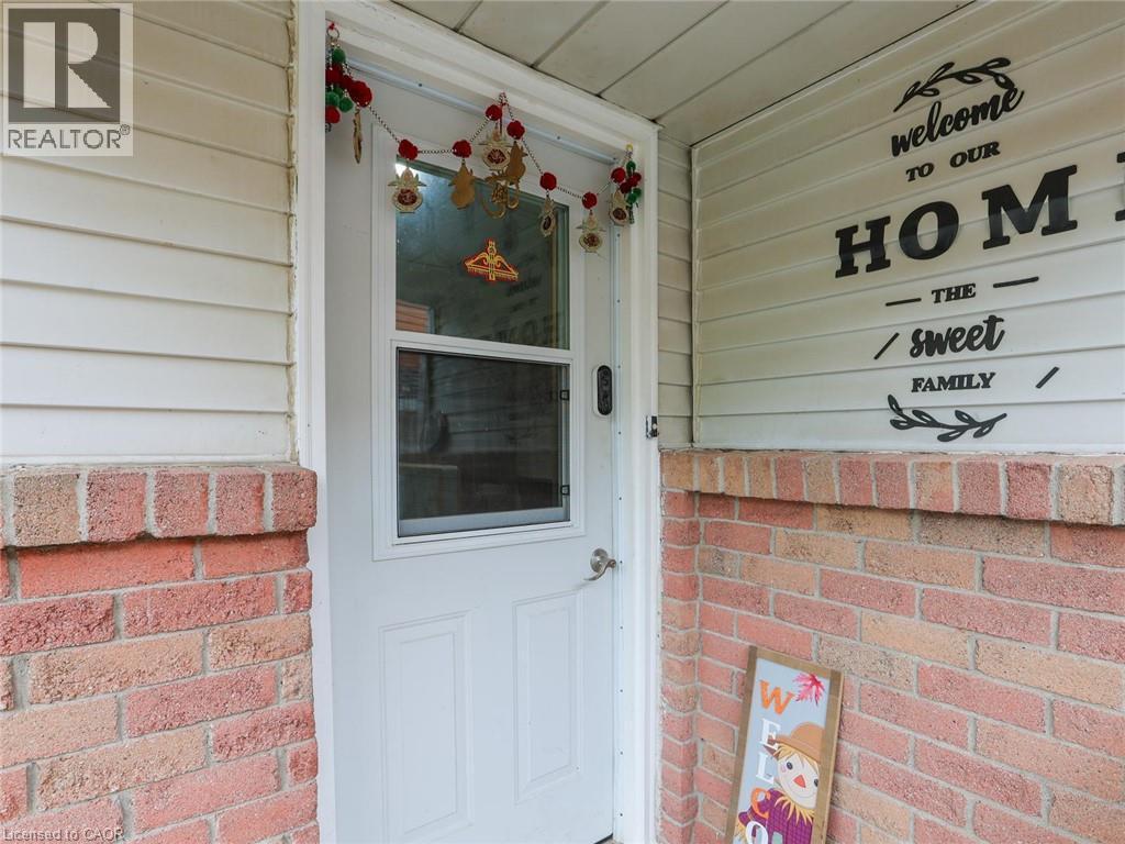 Welcoming entry featuring a white-painted steel door with window insert, brick facade with contrasting horizontal siding, and decorative seasonal accents above the entrance - 128 Macatee Place, Cambridge, ON - Outdoor With Exterior