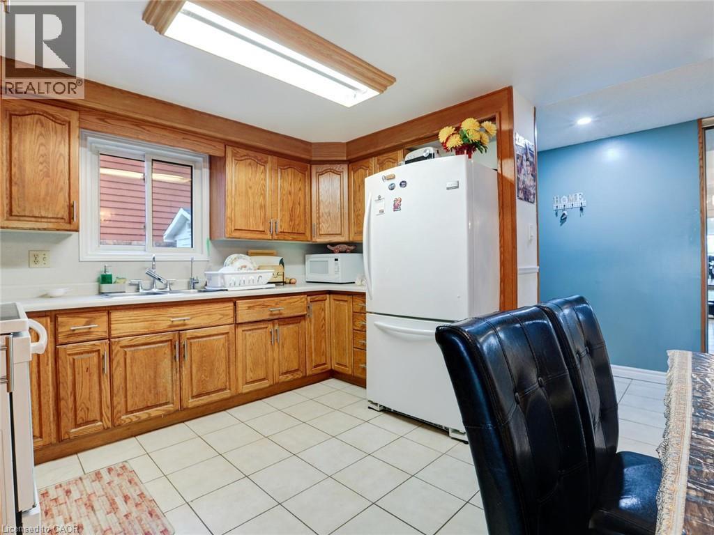 Kitchen featuring wood cabinetry, white countertops, a stainless steel sink, and white tile flooring - 128 Macatee Place, Cambridge, ON - Indoor Photo Showing Kitchen