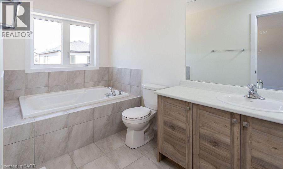 Built-in soaking tub, large window, wood-finish vanity, integrated sink, and tiled flooring - 16 Monteith Drive, Brantford, ON - Indoor Photo Showing Bathroom