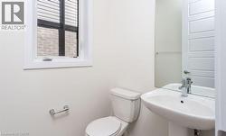 White pedestal sink with chrome faucet, toilet, and a window with horizontal blinds - 