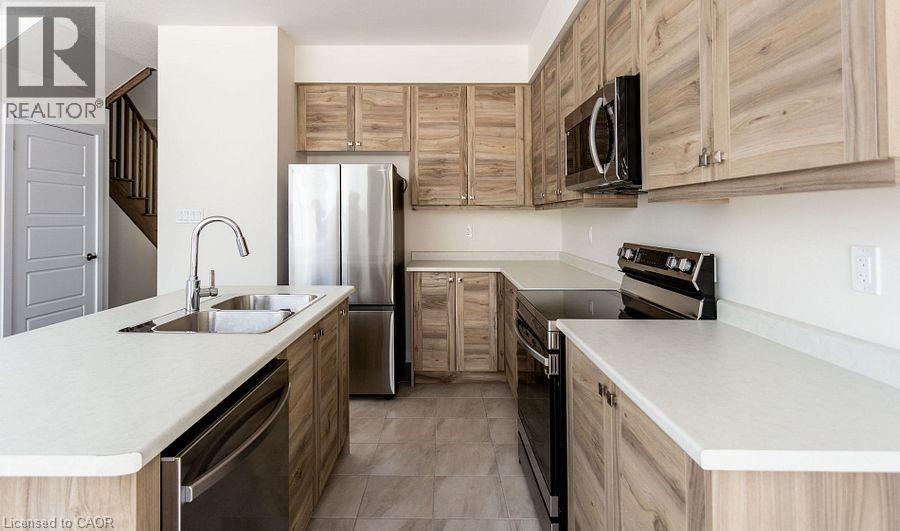 Kitchen featuring wood-finish cabinetry, light-toned countertops, and stainless steel appliances including a refrigerator, dishwasher, and microwave - 16 Monteith Drive, Brantford, ON - Indoor Photo Showing Kitchen With Double Sink
