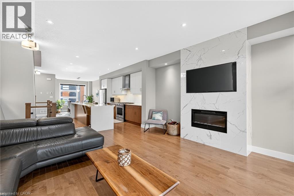 Hardwood-style flooring throughout, kitchen with white and wood-finish cabinetry, built-in stainless steel appliances, and a central island with seating - 60 Arkell Road Unit# 57, Guelph, ON - Indoor Photo Showing Living Room With Fireplace