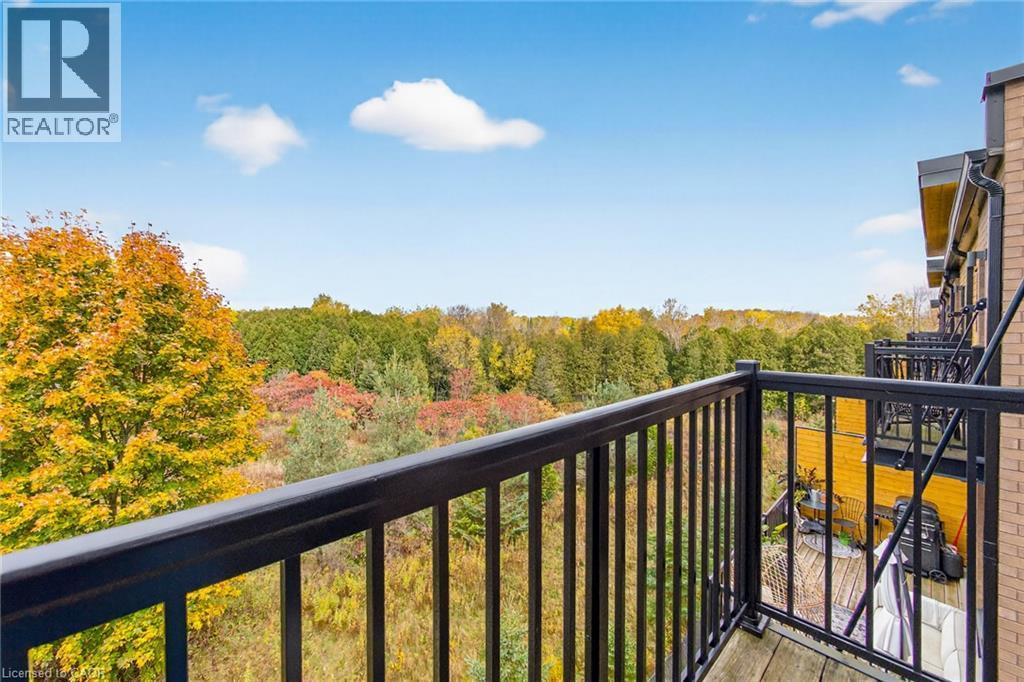 Wood-finish balcony with black metal railings overlooking a dense tree line - 60 Arkell Road Unit# 57, Guelph, ON - Outdoor With Balcony