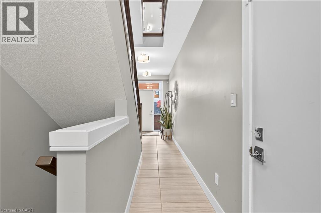 Light-toned wall paint throughout, tile flooring, contemporary wall-mounted light fixtures, and a white stair railing - 60 Arkell Road Unit# 57, Guelph, ON - Indoor Photo Showing Other Room