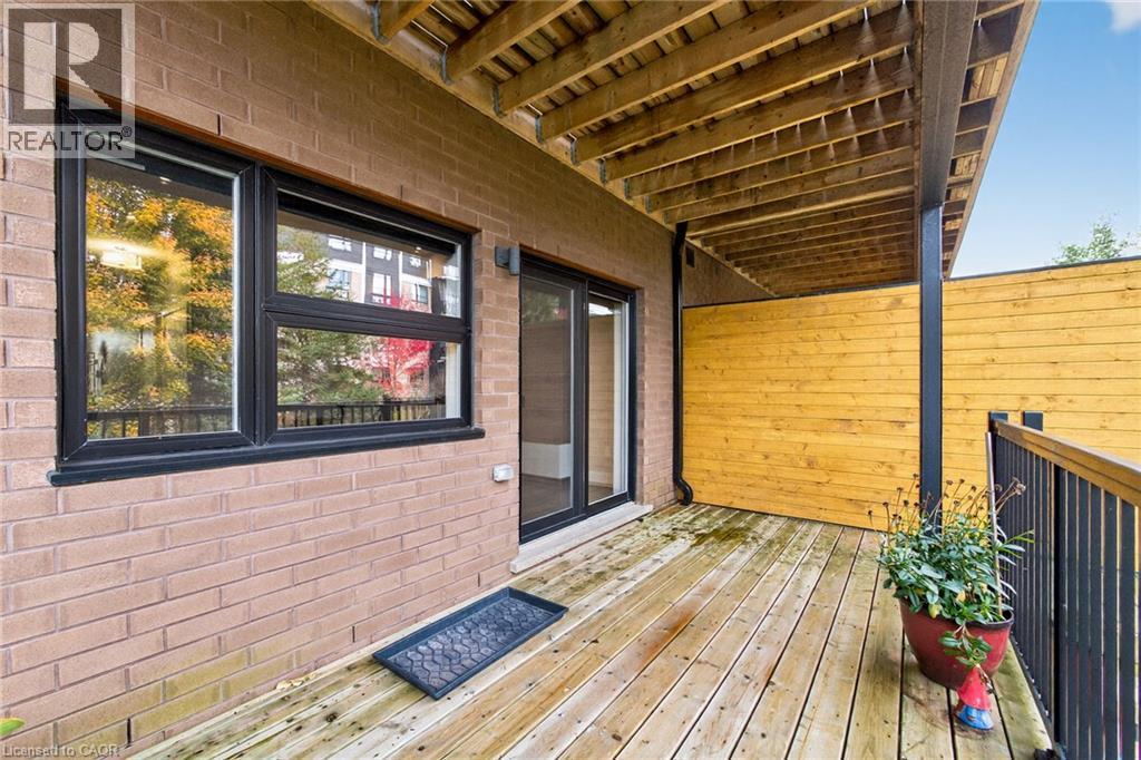 Private wood deck featuring a covered area, black metal railings, a brick exterior wall, and a sliding glass door - 60 Arkell Road Unit# 57, Guelph, ON - Outdoor With Deck Patio Veranda With Exterior