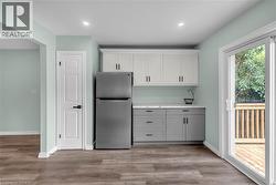 Kitchenette featuring two-tone cabinetry with matte black hardware, a stainless steel refrigerator, and wood-finish flooring - 