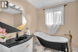 Bathroom featuring a freestanding clawfoot tub with a floor-mounted gold-tone faucet, a white vanity with a black countertop and integrated sink, a geometric mirror with black and gold accents, and pa - 