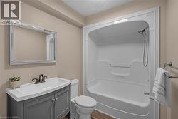 Bathroom with a white fiberglass tub/shower combination, dark gray vanity with white integrated sink, oil-rubbed bronze faucet, and a large framed mirror - 