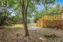Expansive backyard featuring a multi-level wooden deck with lattice skirting, stone paver patio, mature trees, and a perimeter wooden privacy fence - 