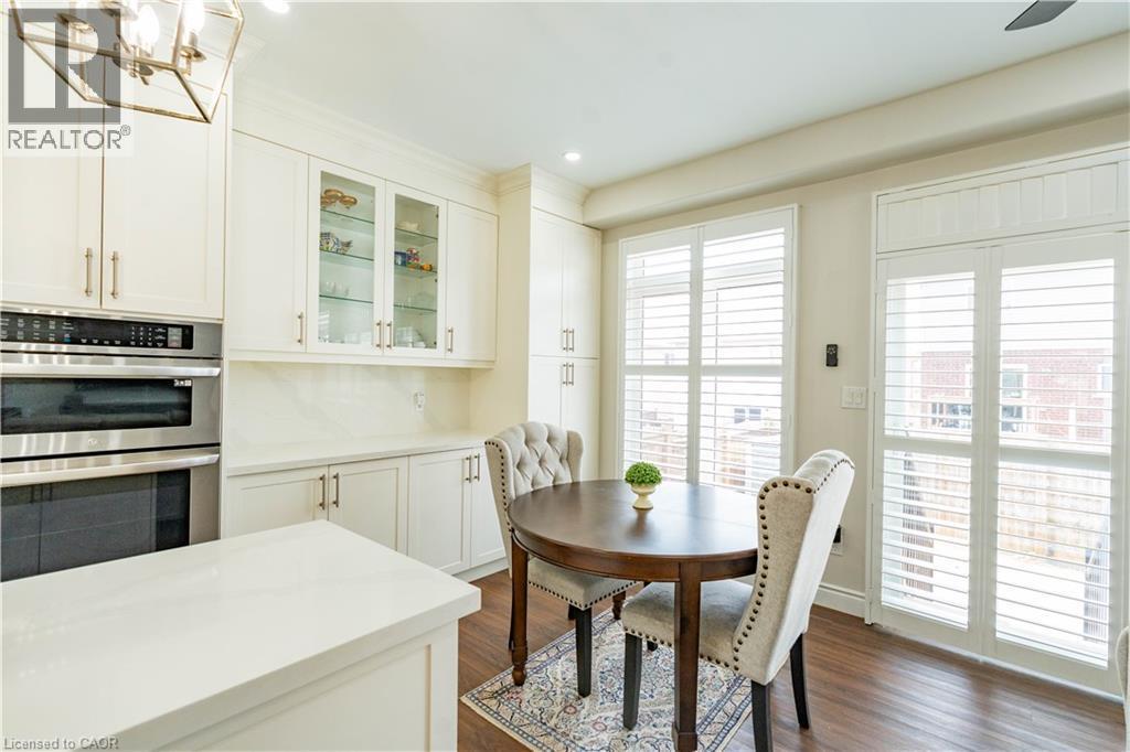 Wood-finish flooring, white cabinetry with glass-front uppers, built-in stainless steel appliances, white countertops, and white plantation shutters - 122 Iron Gate Street, Kitchener, ON - Indoor Photo Showing Dining Room