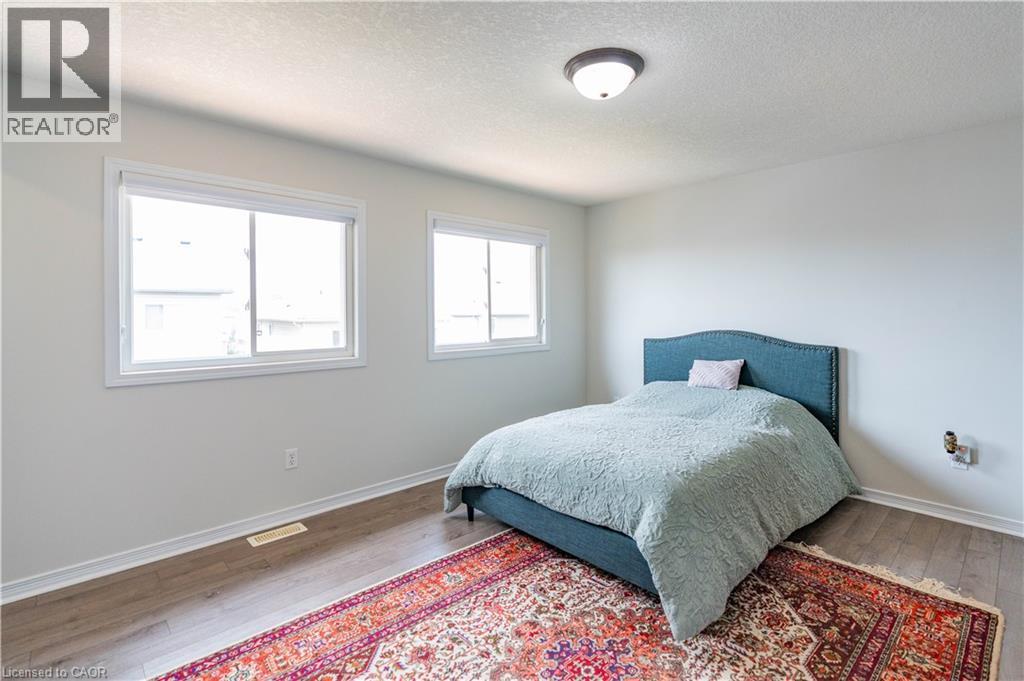 Light-filled room featuring two windows, wood-finish flooring, and a flush mount ceiling light fixture - 122 Iron Gate Street, Kitchener, ON - Indoor Photo Showing Bedroom