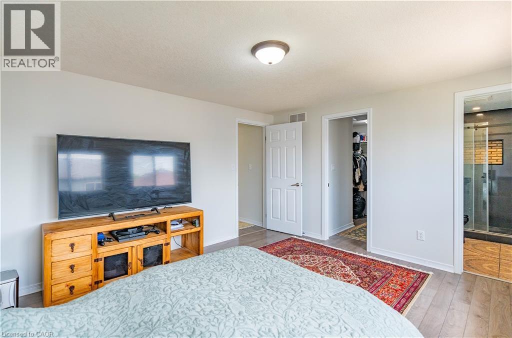 Wood-finish flooring, white painted walls, ceiling-mounted light fixture, open doorway to walk-in closet, and a glass-enclosed shower with tiled walls - 122 Iron Gate Street, Kitchener, ON - Indoor Photo Showing Bedroom