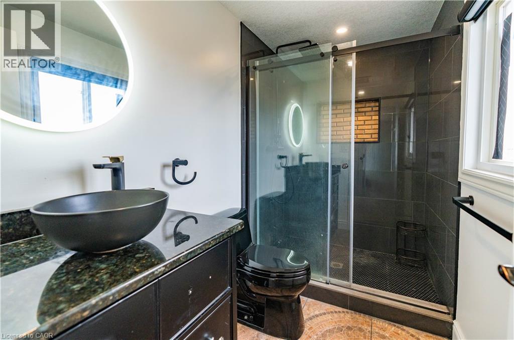 Modern bathroom featuring a vessel sink, dark granite-style countertop, and a glass-enclosed shower with dark tile - 122 Iron Gate Street, Kitchener, ON - Indoor Photo Showing Bathroom