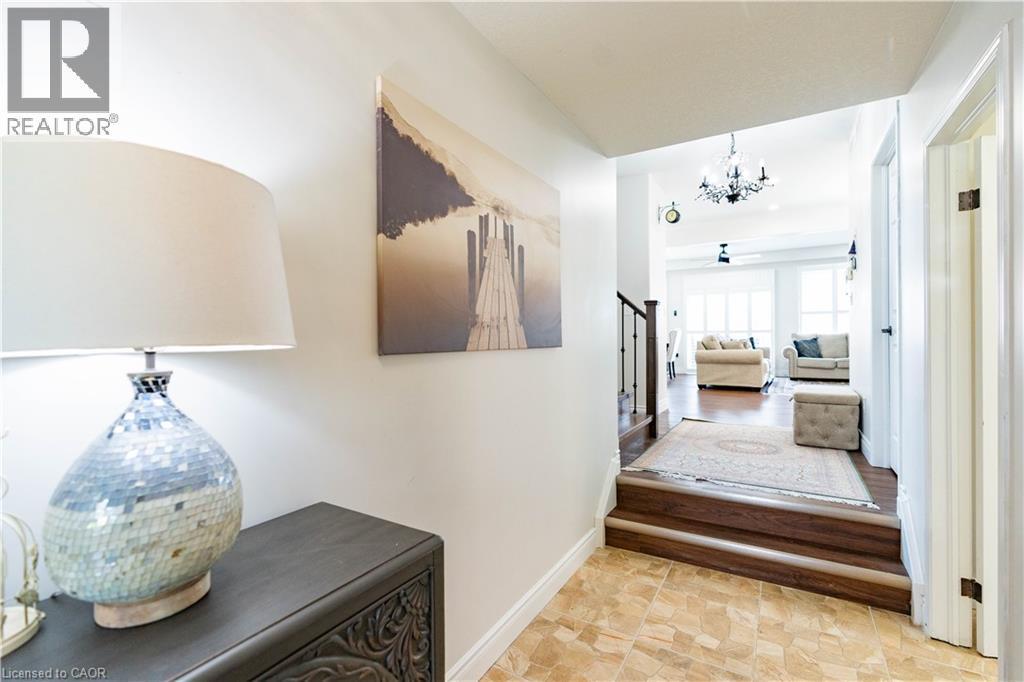 Tiled entry flooring with a wood-finish staircase leading to an open living area featuring wood-finish flooring and a chandelier - 122 Iron Gate Street, Kitchener, ON - Indoor Photo Showing Other Room