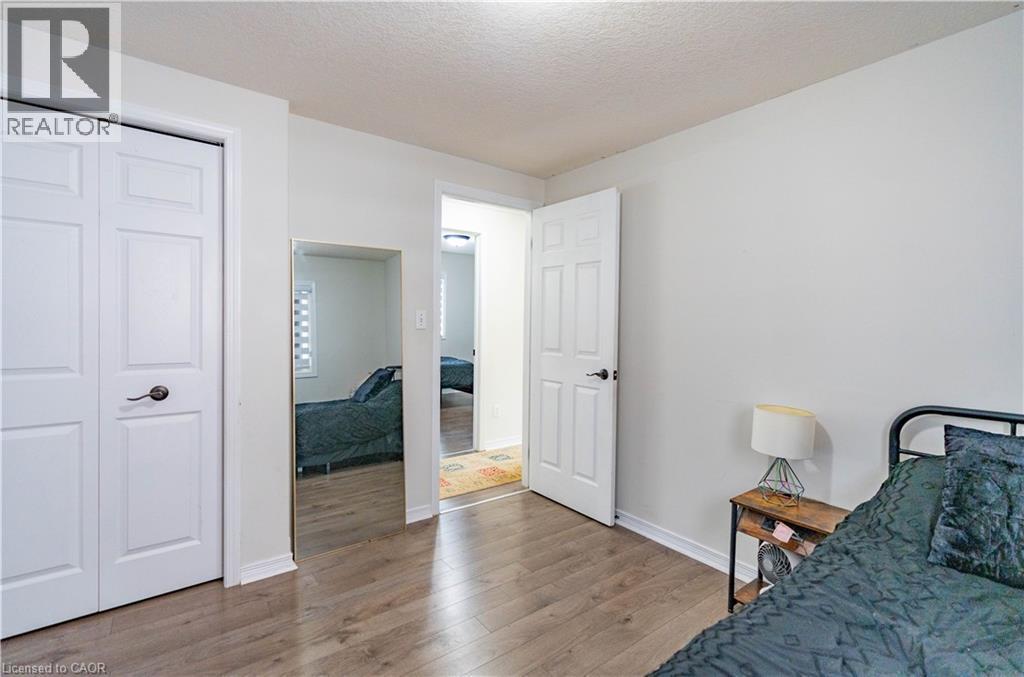 White interior walls, wood-finish flooring, white bi-fold closet doors, white six-panel door, and a full-length wall-mounted mirror - 122 Iron Gate Street, Kitchener, ON - Indoor Photo Showing Bedroom