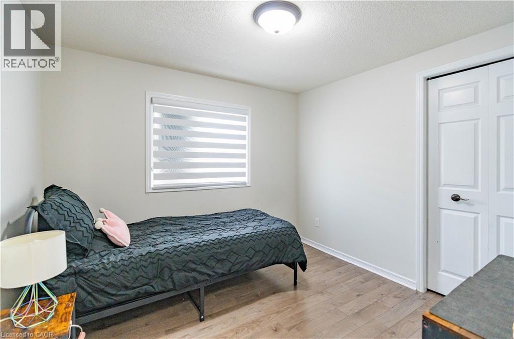 Wood-finish flooring, white walls, flush mount ceiling light, window with blinds, and white bi-fold closet doors - 122 Iron Gate Street, Kitchener, ON - Indoor Photo Showing Bedroom