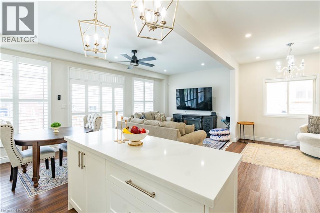 Open-concept living area featuring a large kitchen island with light-toned countertop, wood-finish flooring, recessed lighting, and decorative light fixtures - 122 Iron Gate Street, Kitchener, ON - Indoor
