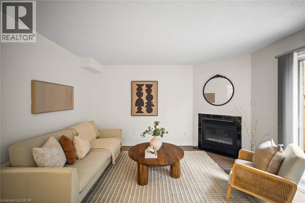 Fireplace with black tile surround, wood-finish flooring, white walls, and sliding glass door - 320 Hamilton Drive Unit# 10, Ancaster, ON - Indoor Photo Showing Living Room With Fireplace