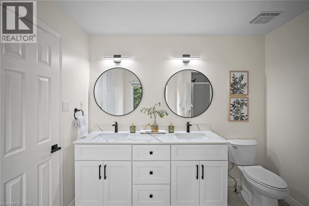 Dual vanity with white cabinetry, integrated sinks, black hardware, and round frameless mirrors - 320 Hamilton Drive Unit# 10, Ancaster, ON - Indoor Photo Showing Bathroom
