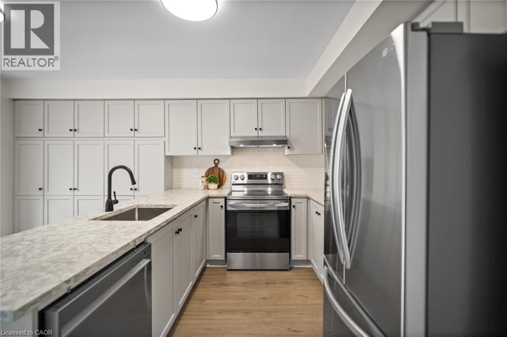 Kitchen featuring light-toned cabinetry, light-toned countertops, stainless steel appliances, a subway tile backsplash, and wood-finish flooring - 320 Hamilton Drive Unit# 10, Ancaster, ON - Indoor Photo Showing Kitchen With Upgraded Kitchen