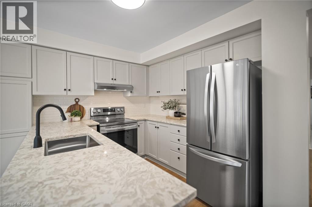 Updated kitchen featuring light-toned cabinetry, light-toned countertops, a stainless steel sink with a matte black faucet, a white subway tile backsplash, and stainless steel appliances - 320 Hamilton Drive Unit# 10, Ancaster, ON - Indoor Photo Showing Kitchen With Double Sink With Upgraded Kitchen