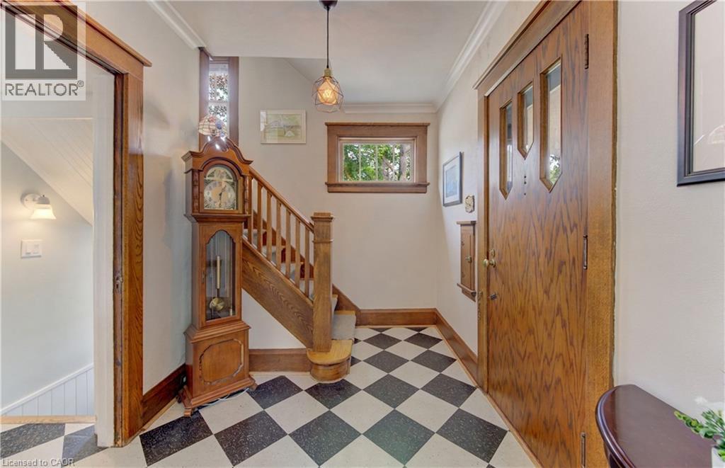 Black and white checkered floor tiling, wood staircase with classic balusters, wood-framed window, natural wood paneled door with integrated glass, and a decorative pendant light fixture - 150 Union Boulevard, Kitchener, ON - Indoor Photo Showing Other Room
