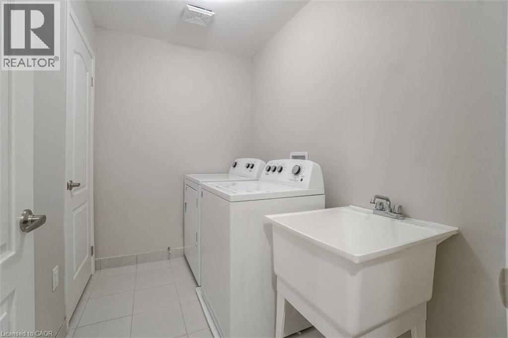 Laundry area with white appliances, utility sink, and light-toned tile flooring - 70 Bradbury Road, Hamilton, ON - Indoor Photo Showing Laundry Room