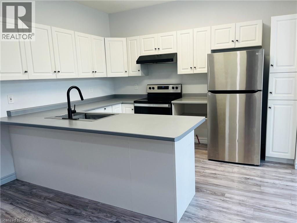 White shaker-style cabinetry with dark hardware, stainless steel refrigerator, black range and hood, integrated sink with matte black faucet, and wood-finish flooring - 83 Keewatin Avenue, Kitchener, ON - Indoor Photo Showing Kitchen