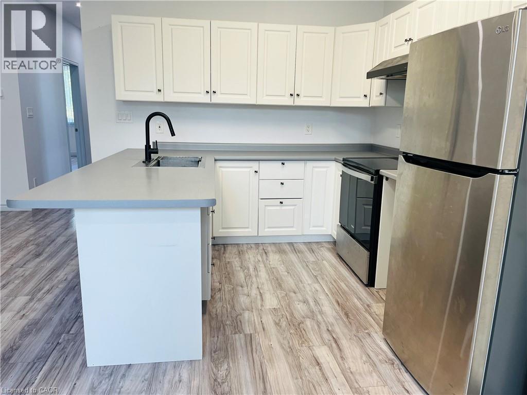 Kitchen featuring white cabinetry, light gray countertops, wood-finish flooring, a stainless steel refrigerator, and a black matte faucet - 83 Keewatin Avenue, Kitchener, ON - Indoor Photo Showing Kitchen