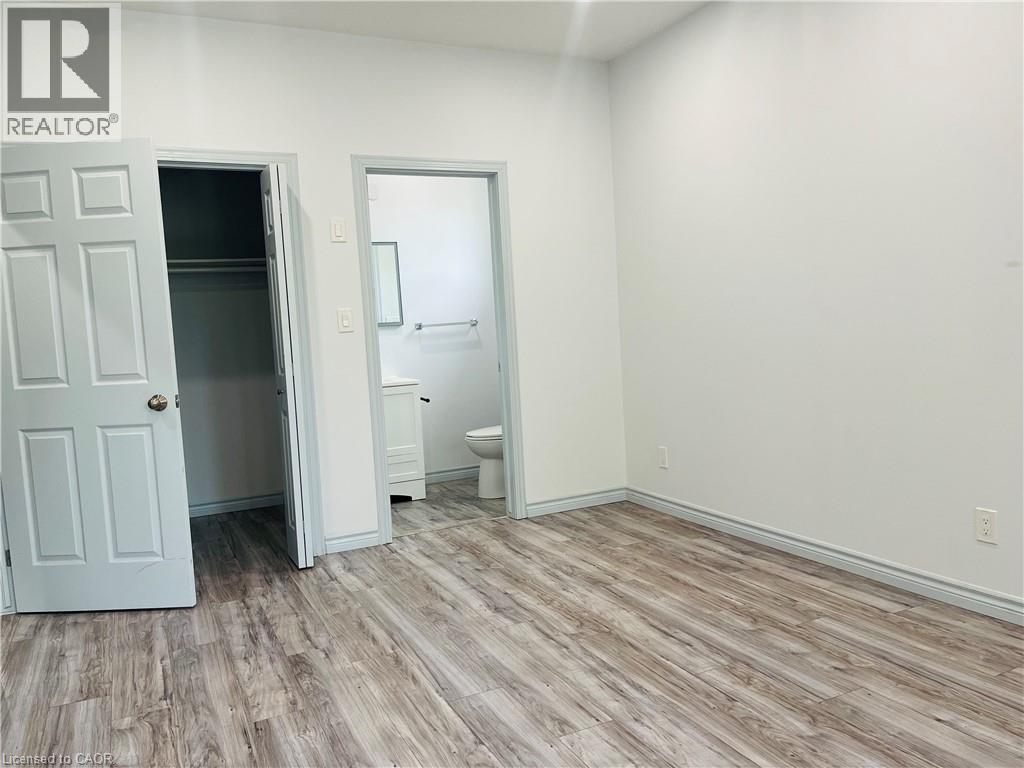 Wood-finish flooring, white walls, and a built-in closet with an adjacent bathroom featuring a vanity and toilet - 83 Keewatin Avenue, Kitchener, ON - Indoor Photo Showing Other Room
