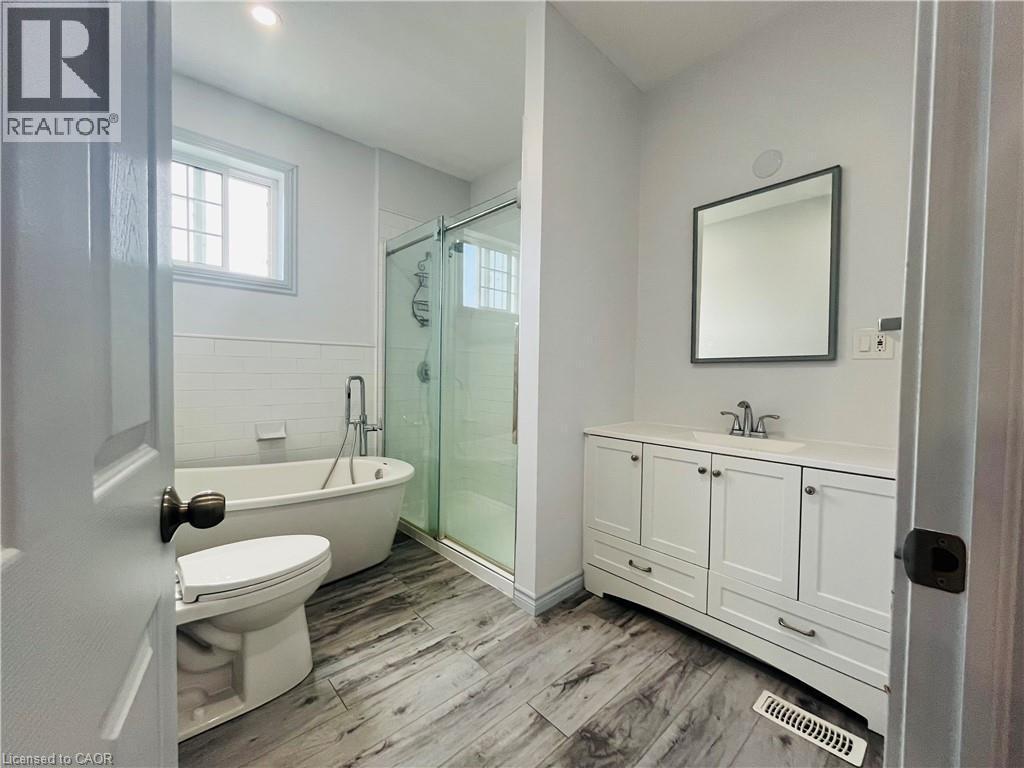 Freestanding soaking tub, glass-enclosed shower, wood-finish flooring, white vanity with integrated sink, and a framed wall mirror - 83 Keewatin Avenue, Kitchener, ON - Indoor Photo Showing Bathroom