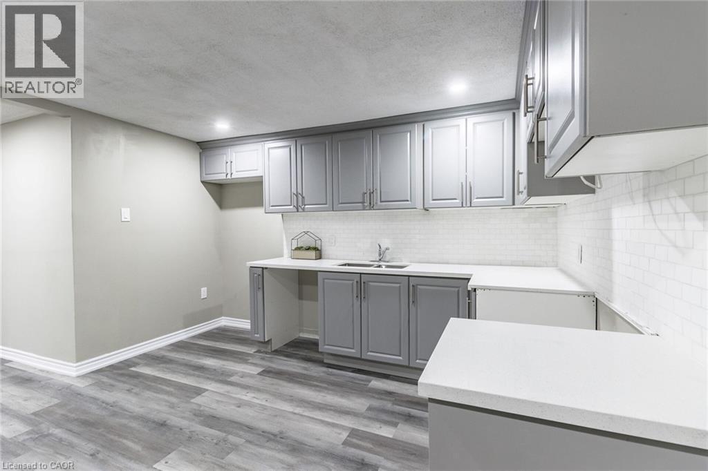 Gray shaker-style cabinetry, white countertops, subway tile backsplash, stainless steel sink, and wood-finish flooring - 15 Spiers Crescent, Cambridge, ON - Indoor Photo Showing Kitchen