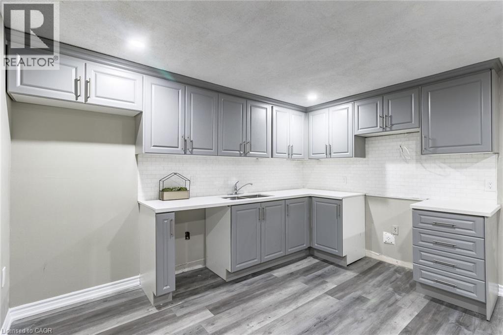 Grey shaker-style cabinetry with chrome hardware, white solid surface countertops, white subway tile backsplash, stainless steel sink, and wood-finish flooring - 15 Spiers Crescent, Cambridge, ON - Indoor Photo Showing Kitchen