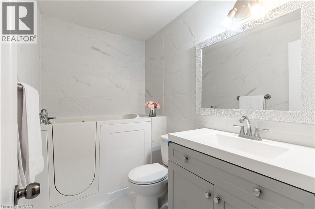Walk-in tub, wall-mounted white tile, framed mirror, vanity with integrated sink, and chrome fixtures - 15 Spiers Crescent, Cambridge, ON - Indoor Photo Showing Bathroom